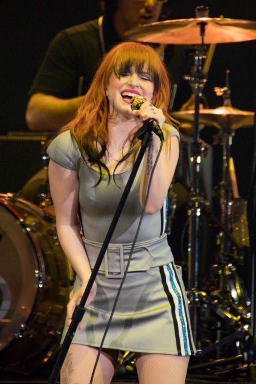 Hayley Williams of the rock band Paramore performs on stage during the 2023 Bud Light Super Bowl Music Festival holding the mic stand wearing a grey dress with blue white and black stripes on the sides.