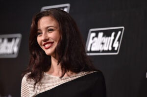 Katie Findlay attends the Fallout 4 video game launch event smiling looking left wearing a white and black dress.