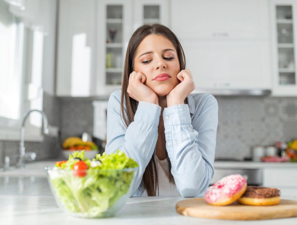 Teenage girl chooses between donuts and vegetable salad