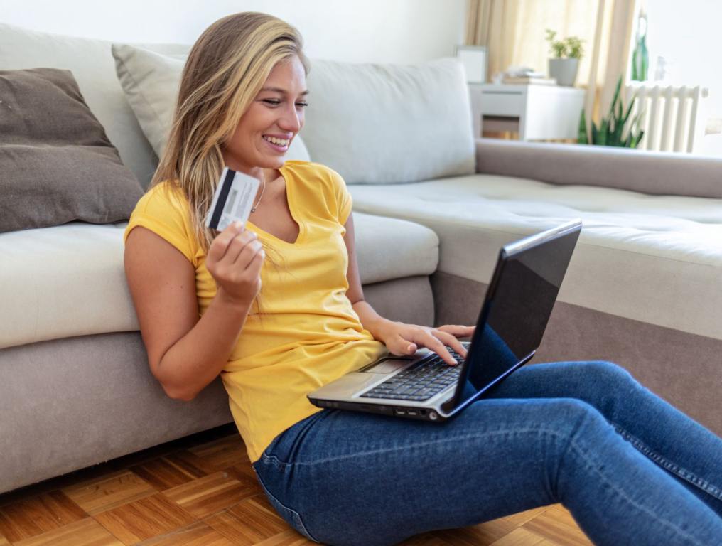 Woman sitting on the floor purchasing something with a credit card. This story is on credit card debt.