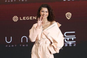 Zendaya attends the press conference for "Dune: Part Two" smiling wearing a pink leather jumpsuit.