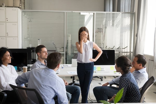 Shy nervous bashful female employee feels embarrassed blushing afraid of public speaking at corporate group team meeting, timid stressed woman hiding face during awkward moment reporting in office. Corporate jargon