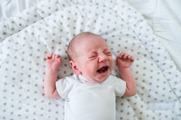 Cute little newborn baby boy lying on bed, crying. Close up. Worst state to have a baby