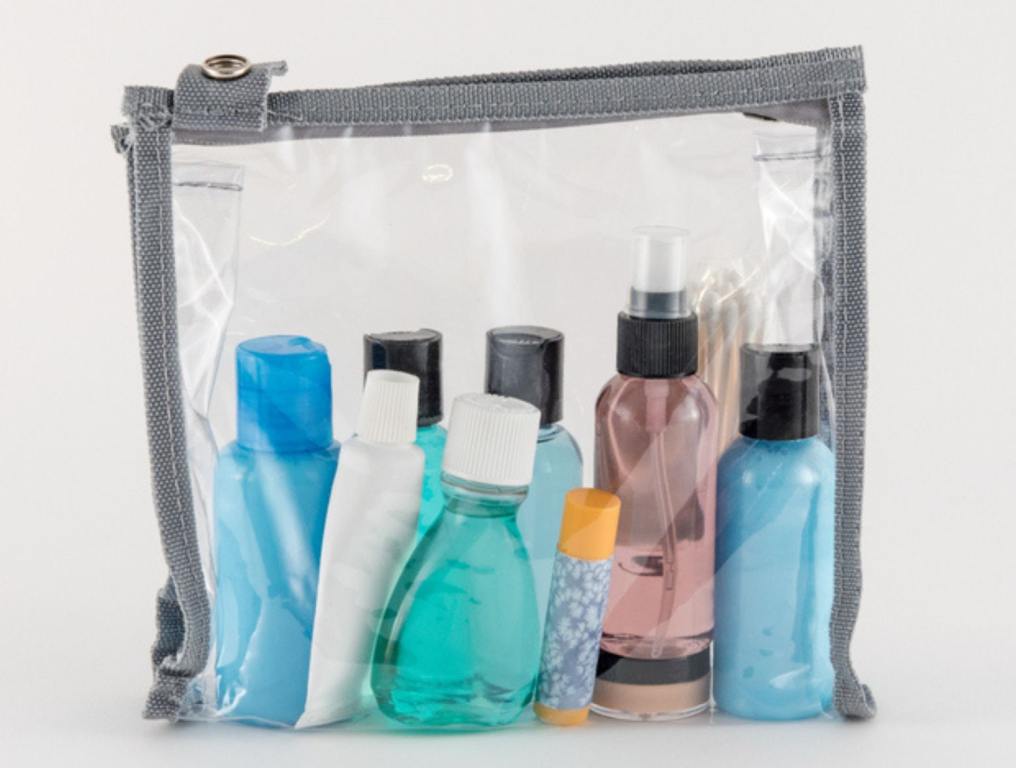 Travel toiletries in clear plastic, quart-sized bag on white background