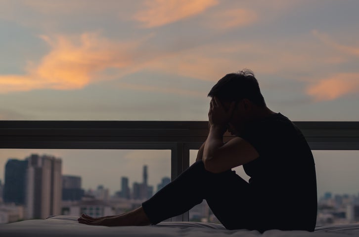 A person sitting and feeling depressed on bed with city view in dusk moment. Stay home, depression and loneliness concept.