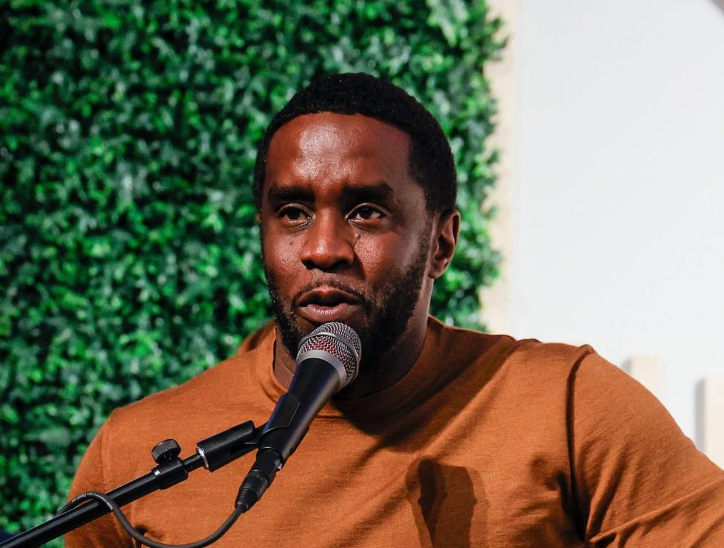 Sean "Diddy" Combs speaks during the National Town Hall looking left wearing a khaki sweater at the podium, Diddy Faces New Sex Trafficking Allegations.