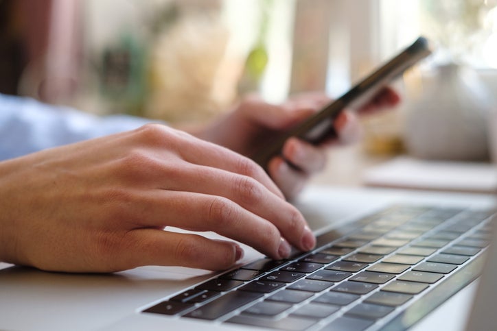 Woman using smart phone and laptop, female hands using smart phone in interior at home, woman at workplace using technology. Female hands on the keyboard. Close up