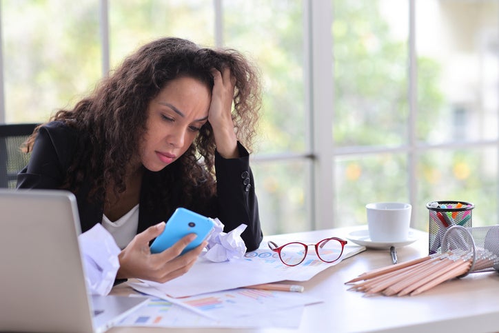 Mid adult businesswoman touching her head with crumpled paper on table in office after bad news business failure or get fired and feeling discouraged, distraught and hopeless in modern office.